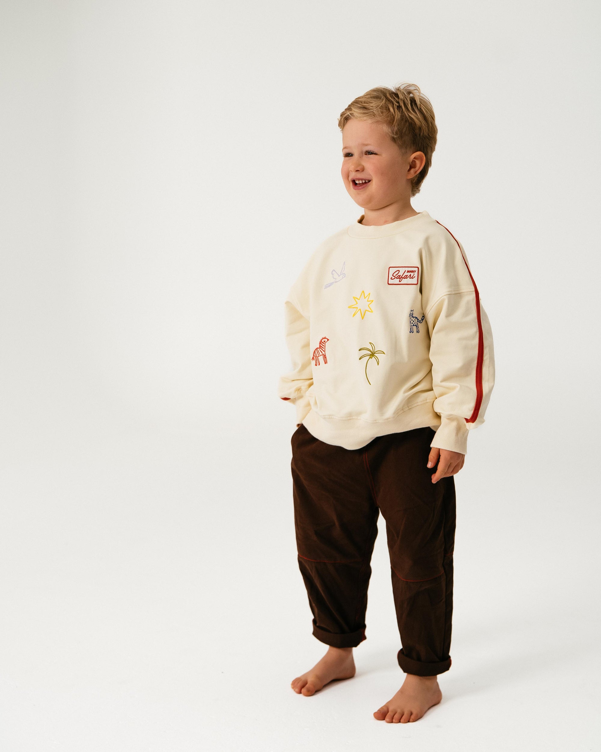 Child wearing a cream-colored sweatshirt with graphics and dark pants on a white background