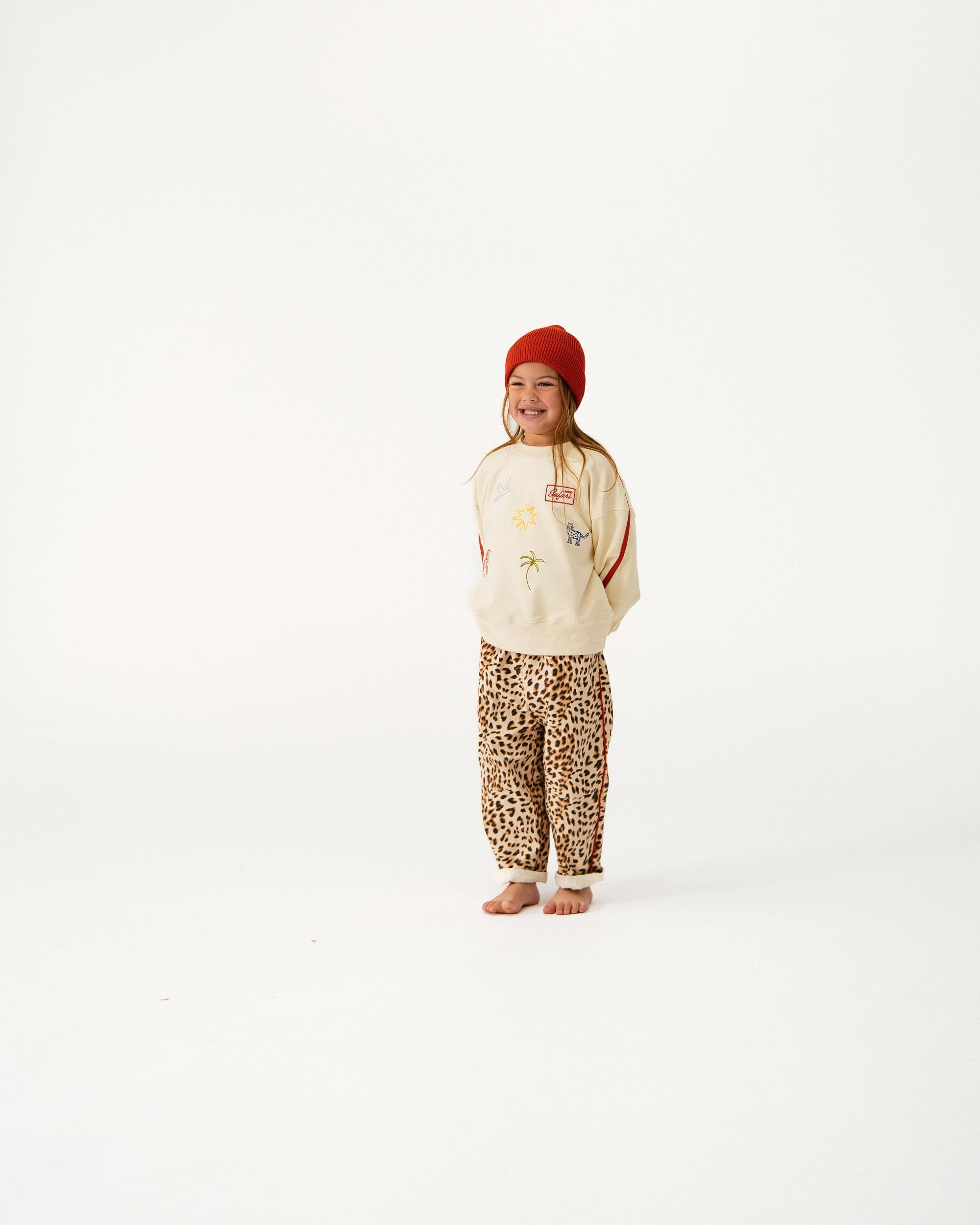 Person wearing a beige sweater with a graphic design, leopard print pants, and a red beanie on a white background