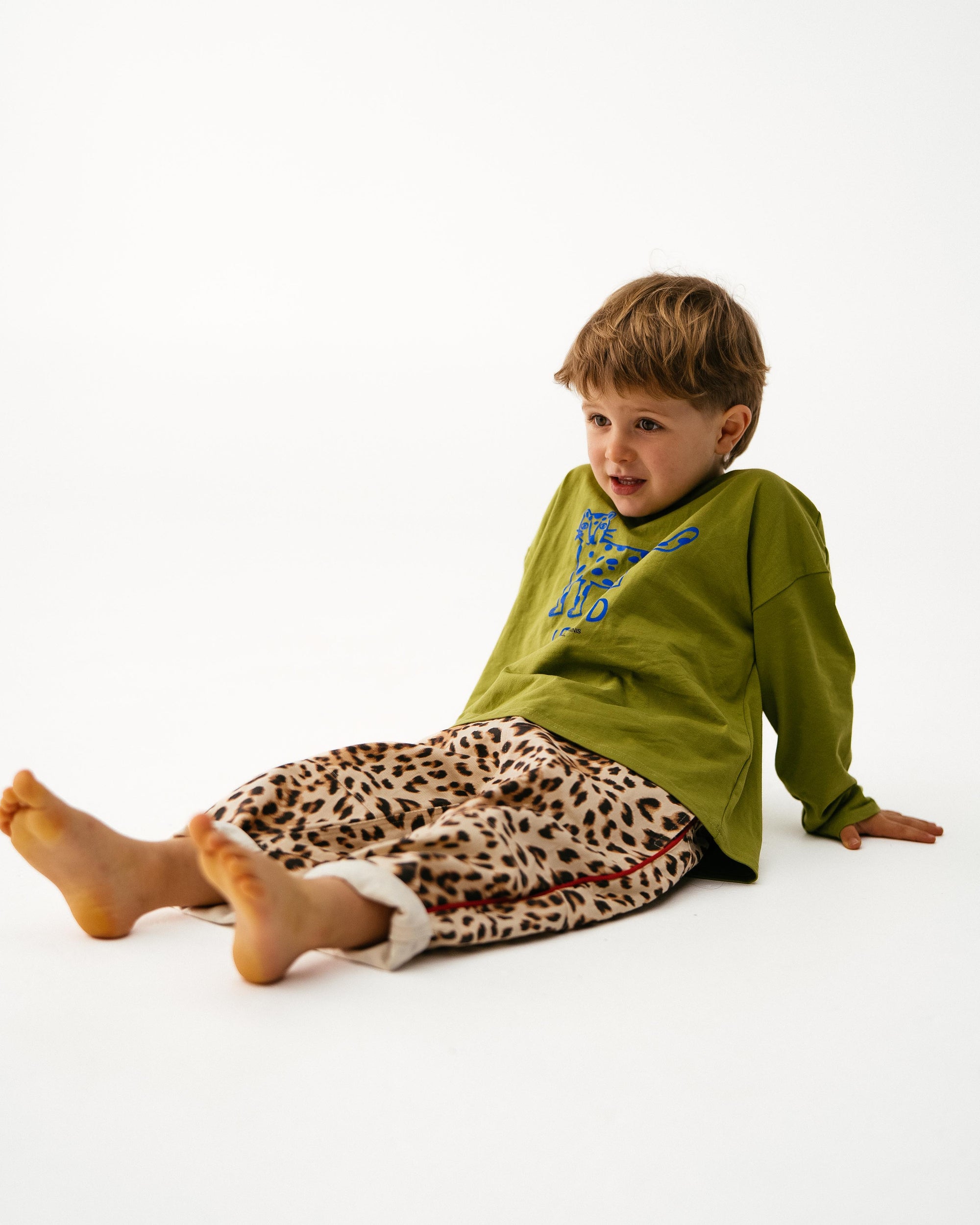 Child wearing a green shirt and leopard print pants sitting on a white background