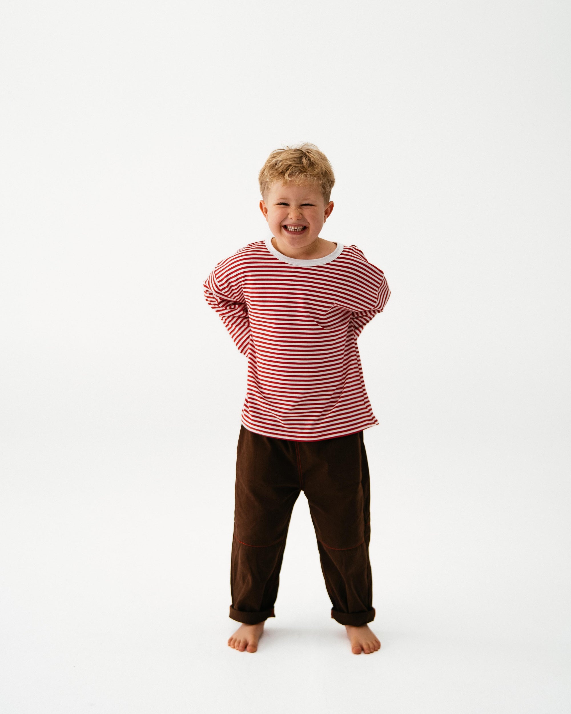 Child wearing a red and white striped shirt and brown pants on a white background