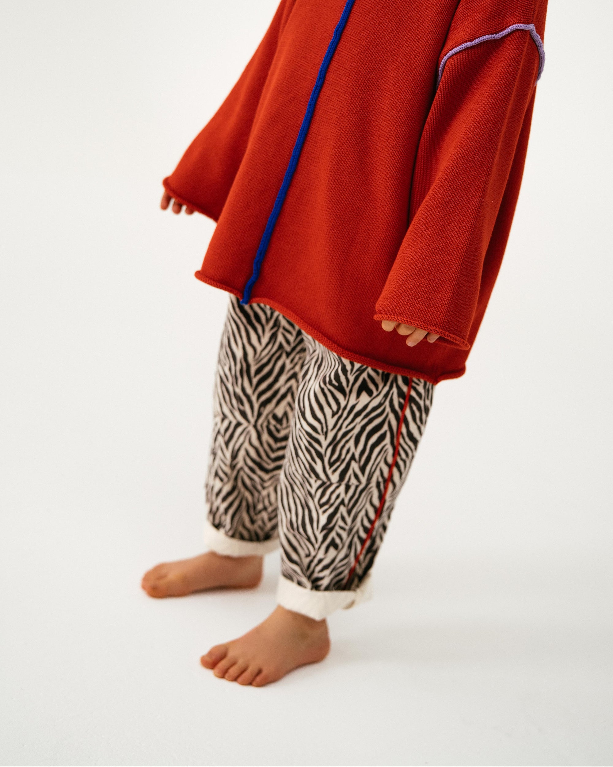 Person wearing a red oversized sweater with blue zipper and zebra print pants on a white background
