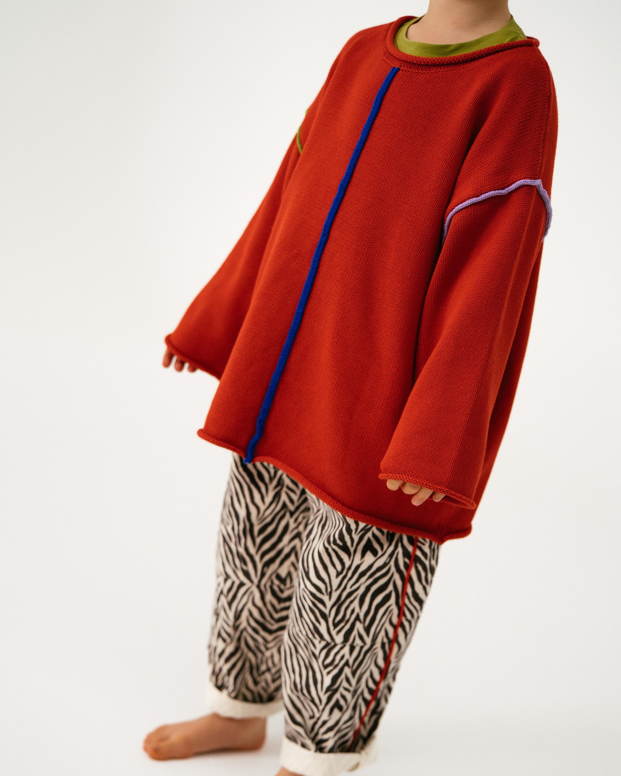 Person wearing a red oversized sweater with blue zipper and zebra print pants on a white background