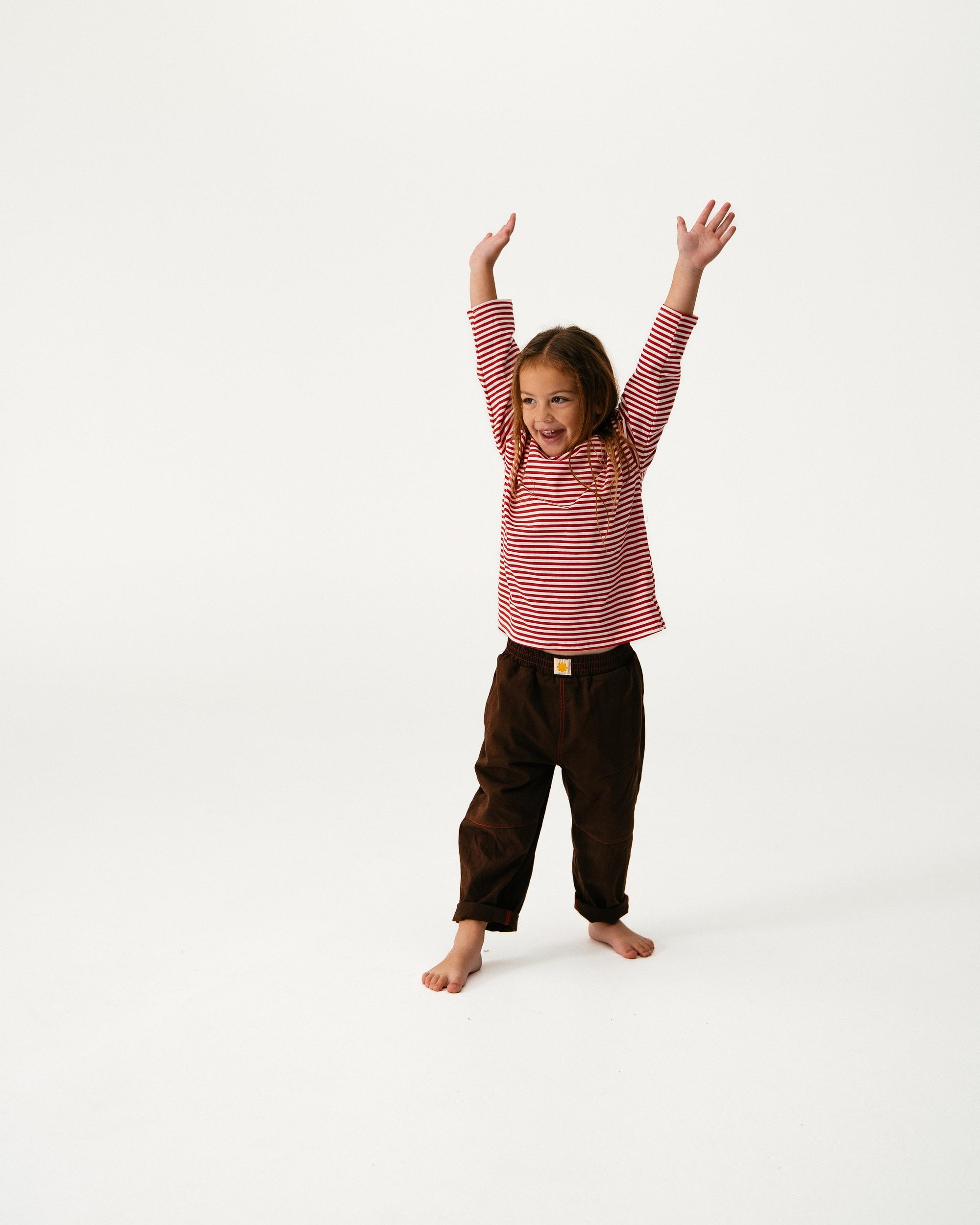Child wearing a red and white striped shirt and brown pants on a white background