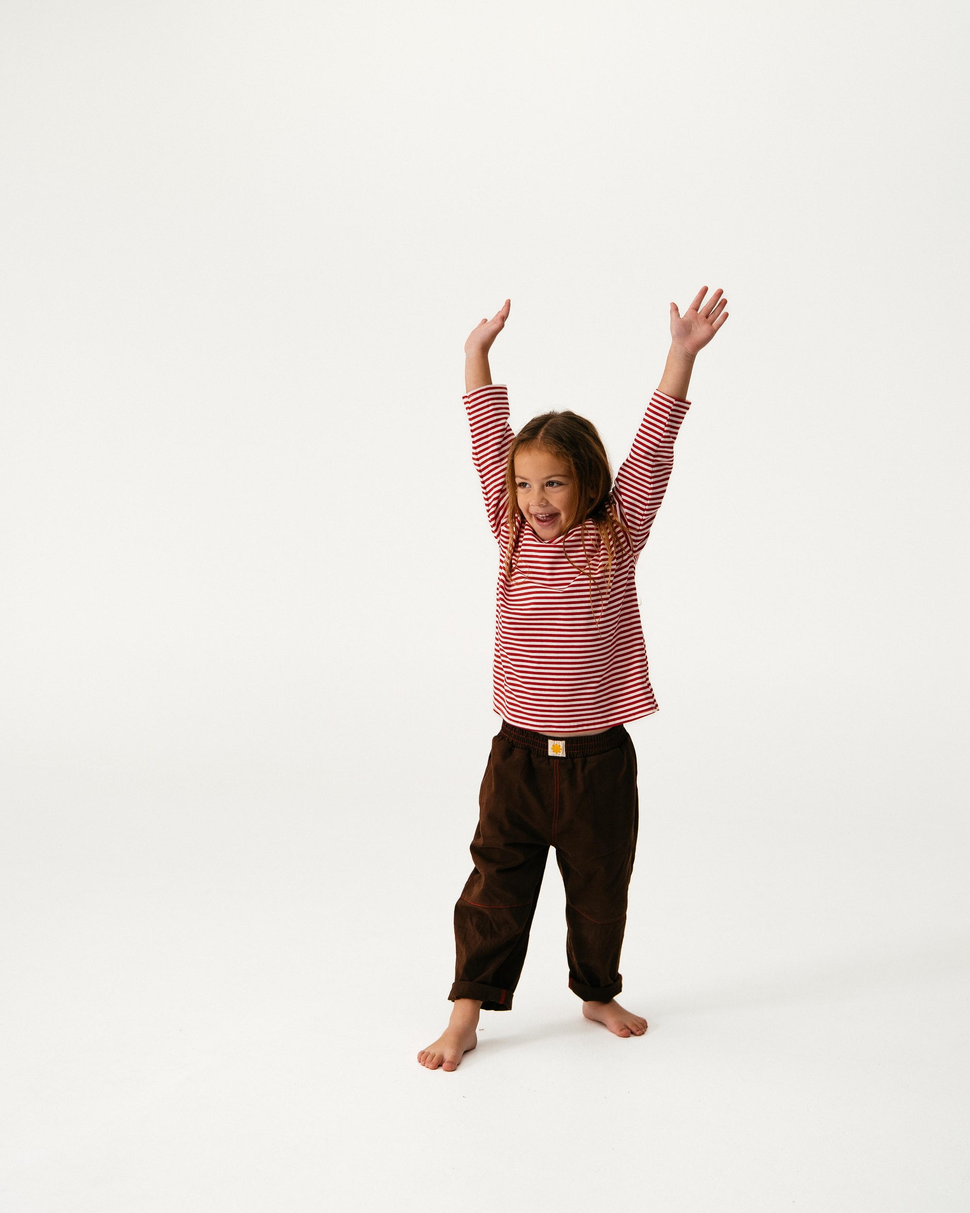 Child wearing a red and white striped shirt and brown pants on a white background