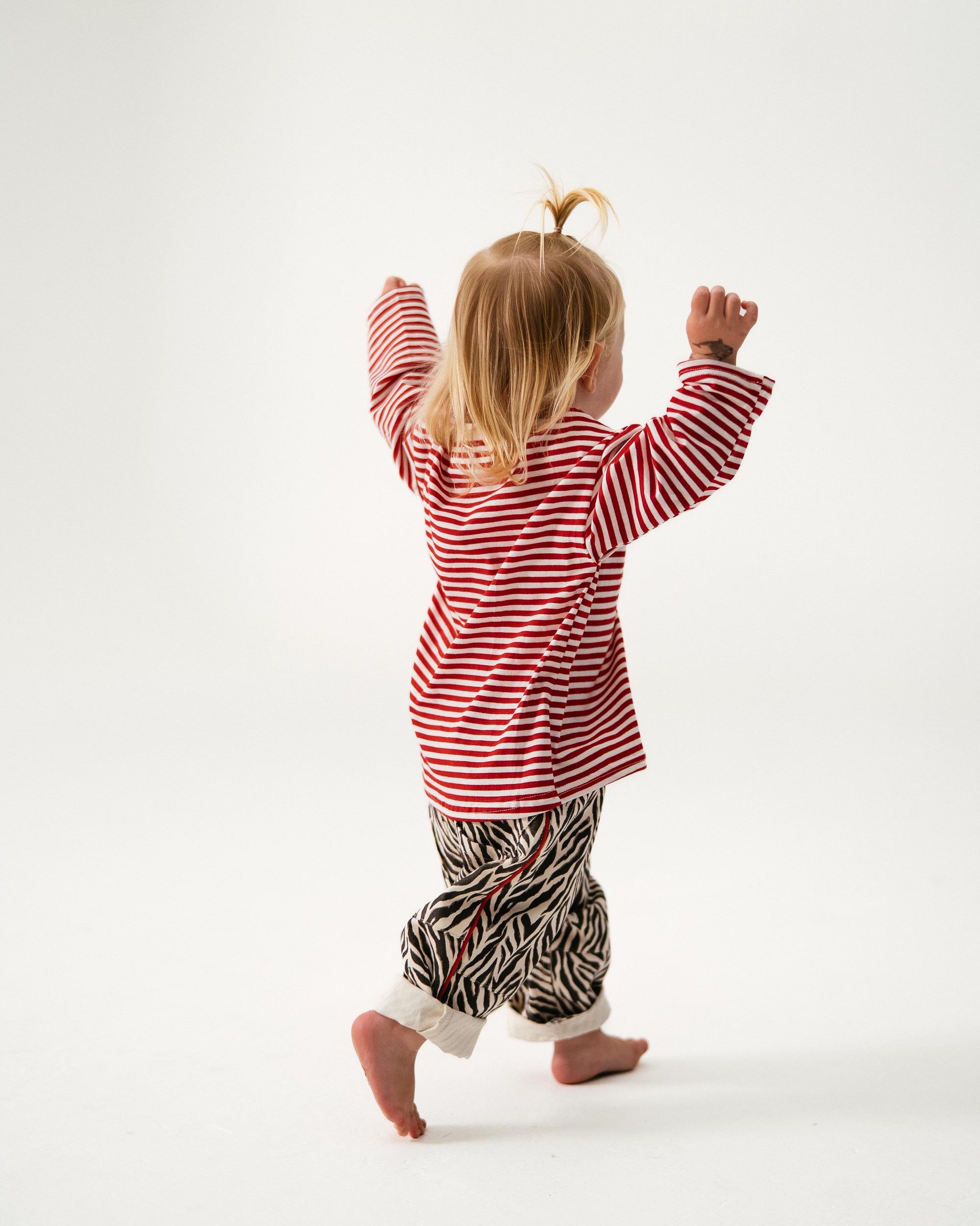 Child wearing a red and white striped shirt and patterned pants on a white background