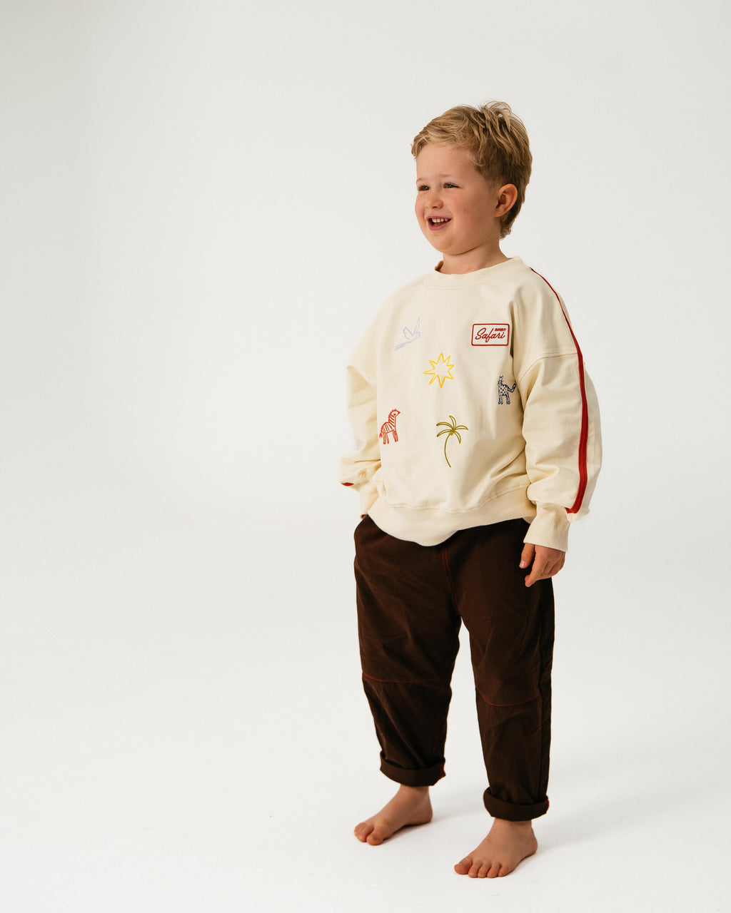 Child wearing a cream-colored sweatshirt with graphics and dark pants on a white background