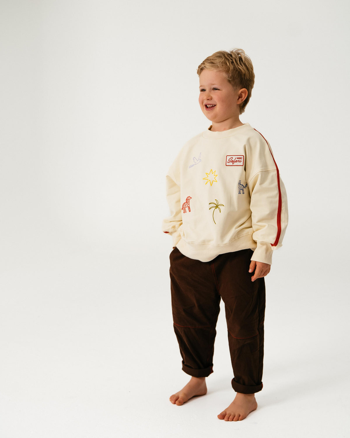 Child wearing a cream-colored sweatshirt with graphics and dark pants on a white background