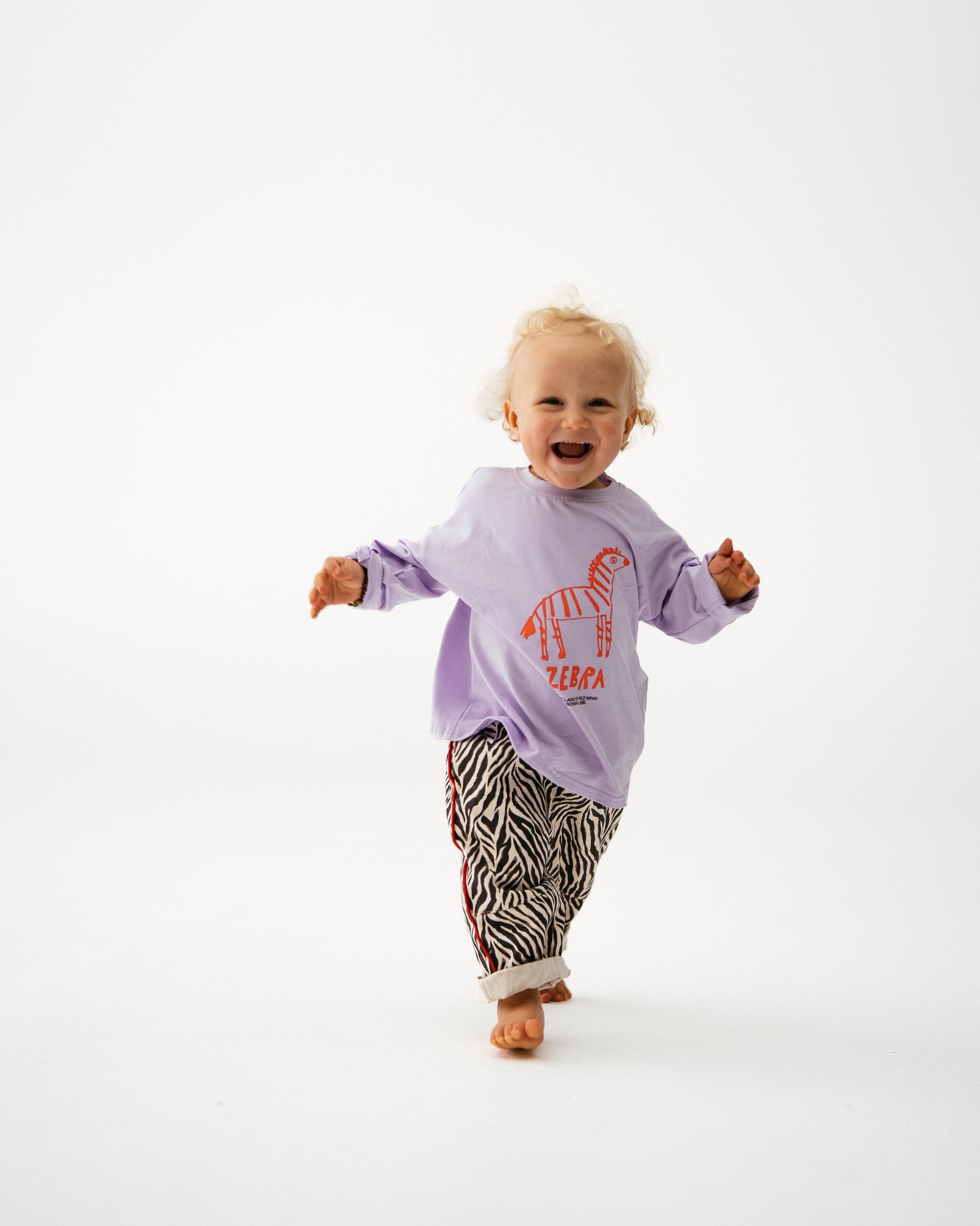 Child wearing a purple sweatshirt with text and zebra print pants on a white background