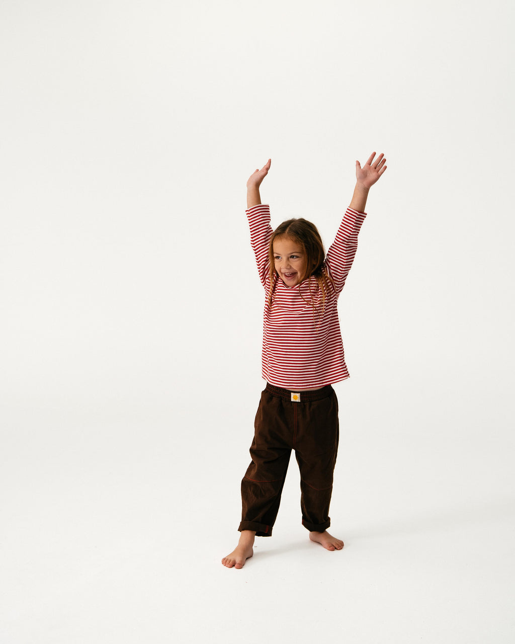 Child wearing a red and white striped shirt and brown pants on a white background