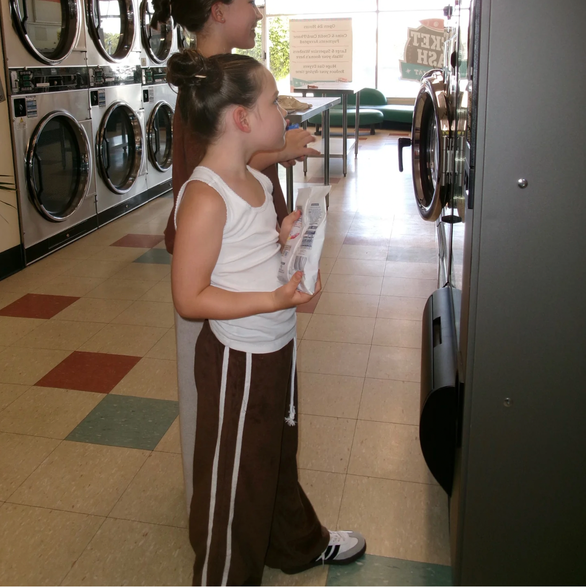 Two individuals standing in a laundry room wearing the Terry Pant in chocolate colour with a white twin stripe on the sides.