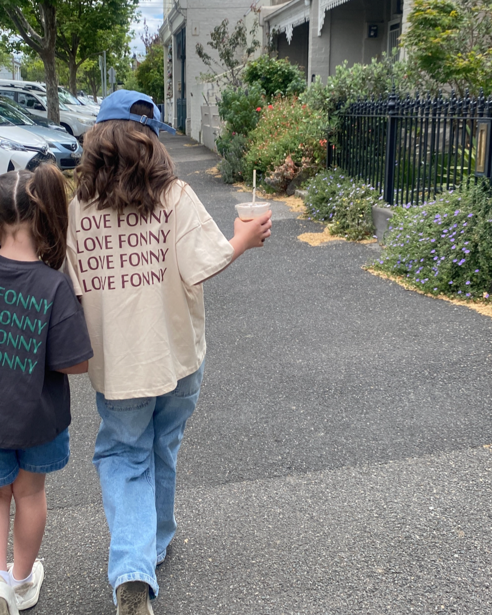 A person wearing a beige 'LOVE FONNY' t-shirt and blue jeans, walking on a street.