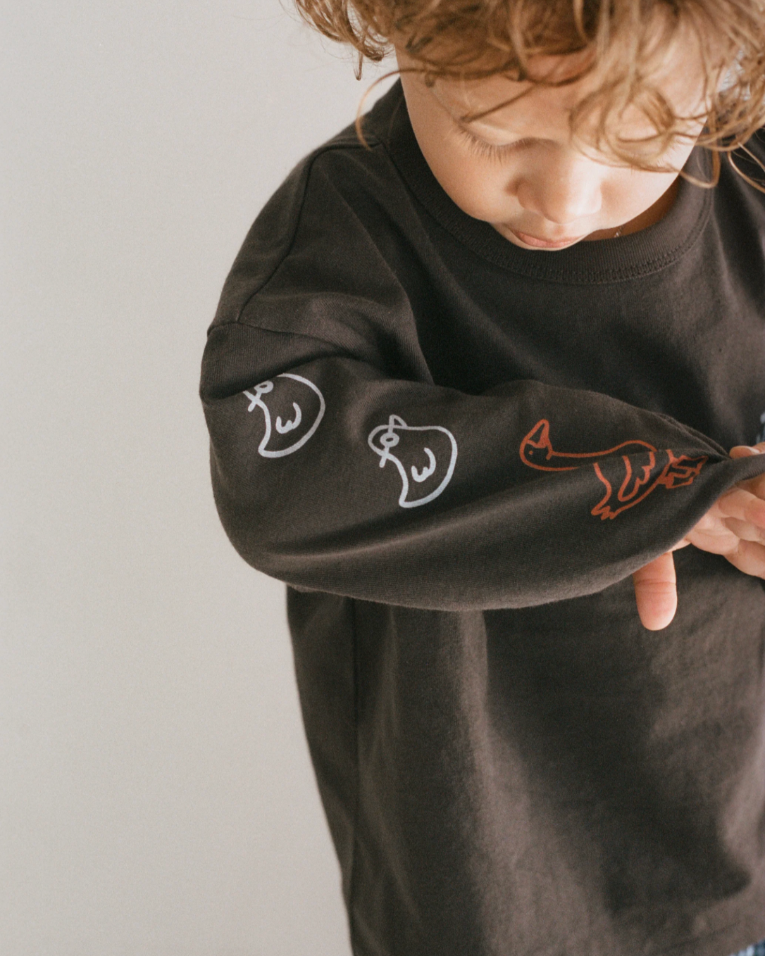 Child wearing a black long-sleeve shirt with animal designs on a plain background